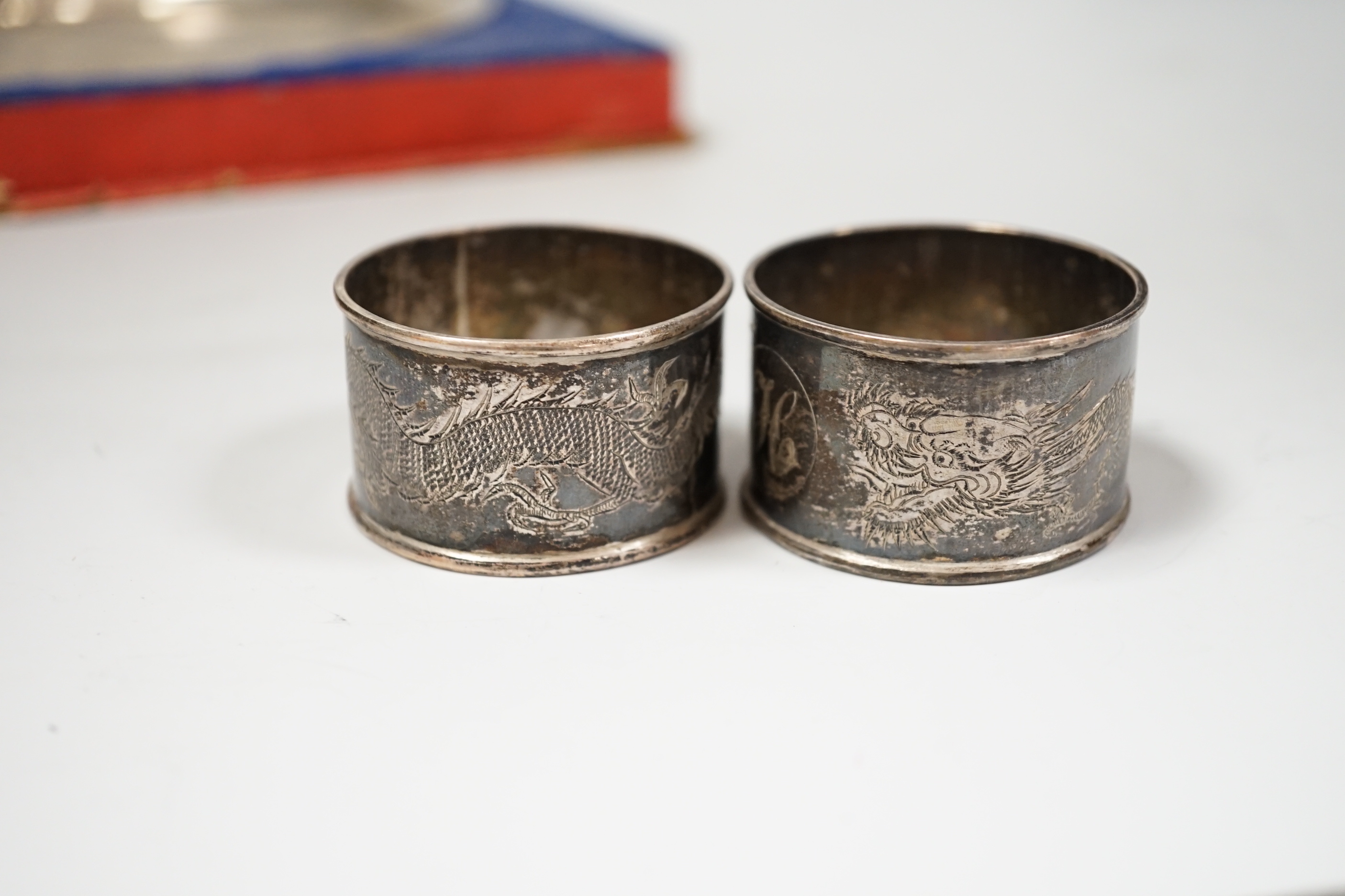 A Chinese white metal ‘dragon’ salver, late 19th century, 20.2cm carded silk box base and two similar napkin rings.